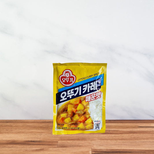 Sachet jaune de préparation pour curry coréen épicé Ottogi 100g avec visuel de plat servi avec riz blanc.