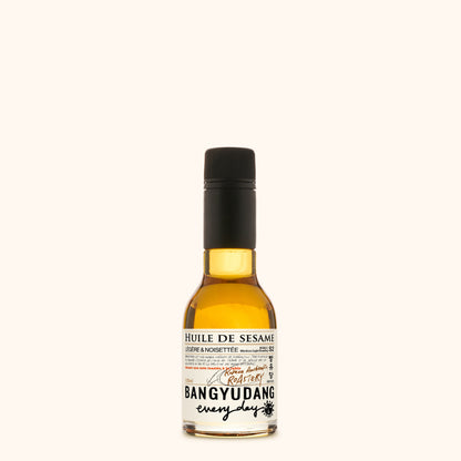Bouteille de 100ml d'huile de sésame douce Bangyudang S2, fond clair, étiquette beige dorée et typographie noire.
