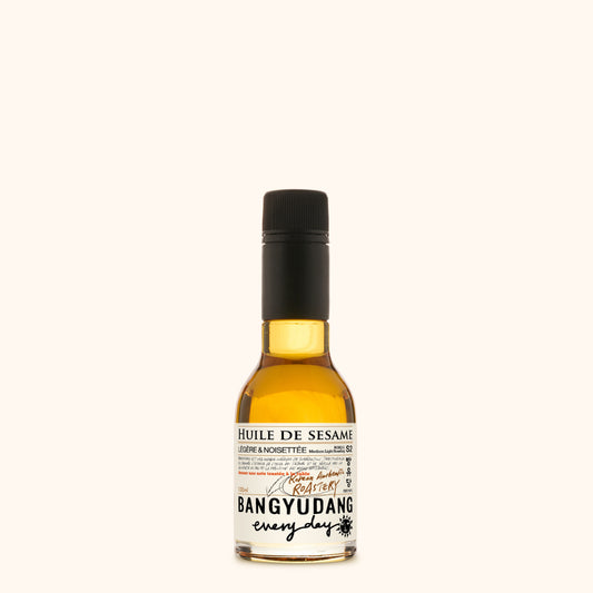 Bouteille de 100ml d'huile de sésame douce Bangyudang S2, fond clair, étiquette beige dorée et typographie noire.
